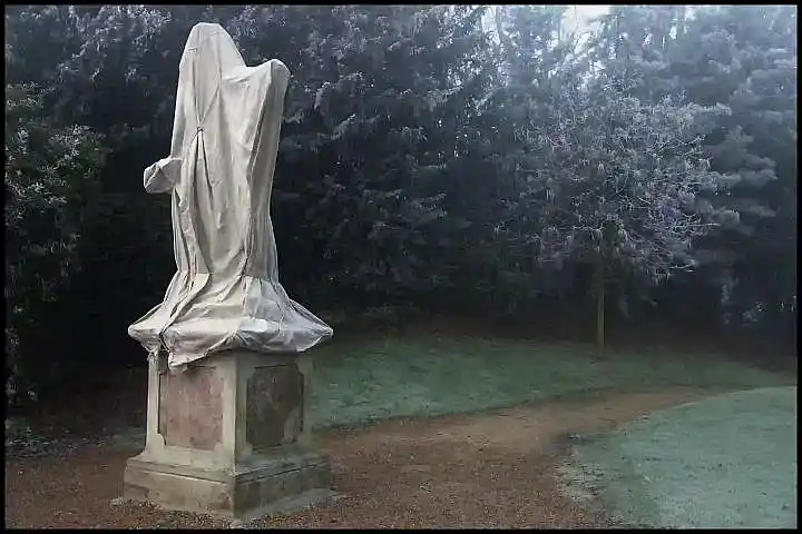 covered statue by a garden path on a frosty morning