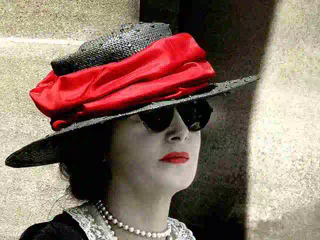 woman in large flamboyant thirties style hat with red band